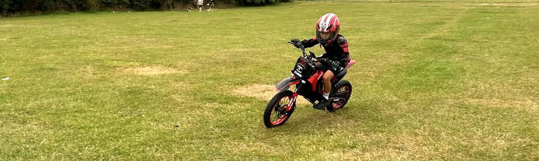 Young child riding a small Kubbi electric dirt bike across a grass lawn