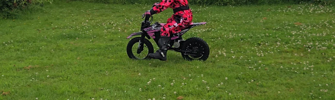 Child in a helmet riding a pink Kubbi electric dirt bike on grass