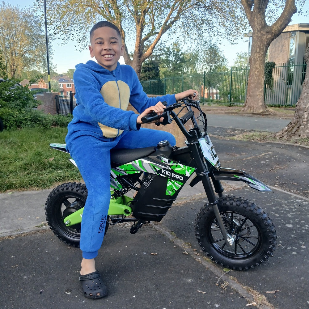 Boy sitting on a green Kubbi electric dirt bike on a driveway