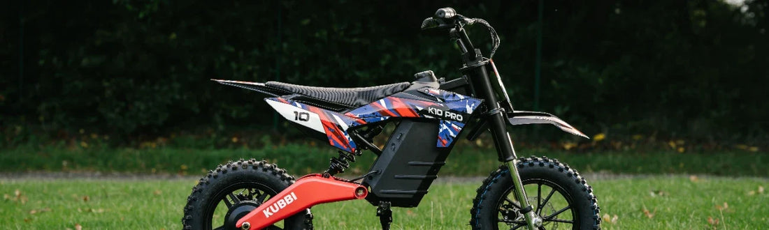 Kubbi K10 Pro kids' electric dirt bike in red, white and blue, side on by a hedge