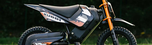 Side view of a Kubbi kids' electric dirt bike in orange and black, showing the frame, forks and seat