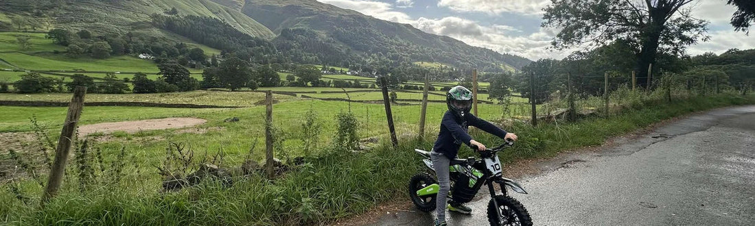 Child riding a Kubbi electric dirt bike in a field with hills behind