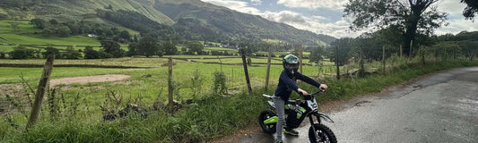 Child riding a Kubbi electric dirt bike in a field with hills behind