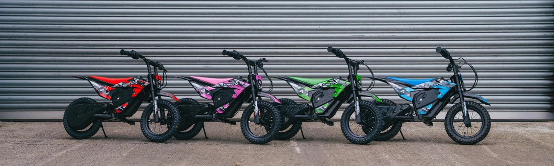 Five Kubbi K4 electric dirt bikes lined up in red, pink, green and blue against a grey shutter