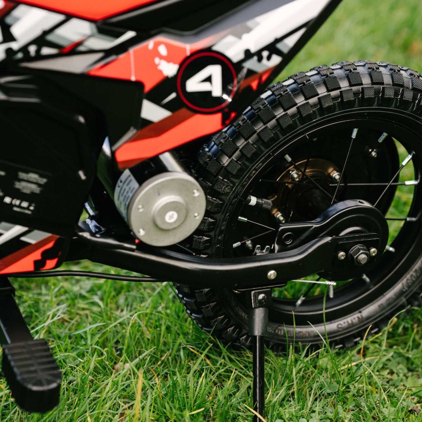 Close-up of Kubbi K4 Dirt Bike rear wheel and motor on grass with off-road tire and kickstand