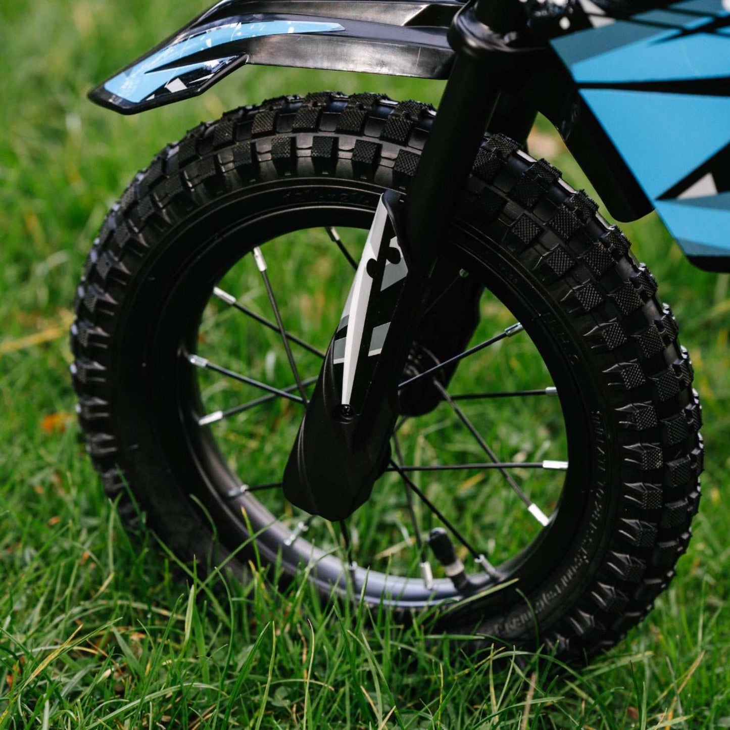 Close-up of Kubbi K4 Dirt Bike 12-inch off-road tire on grass with blue and black frame